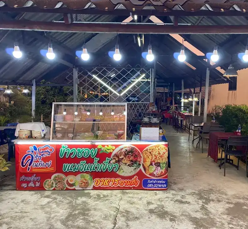 The front counter with its red sign, and tables under the roof behind it, in the evening