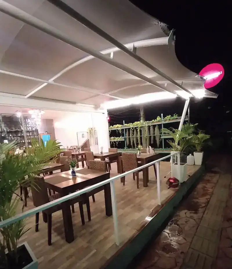 The covered terrace at night, wooden tables under the canopy