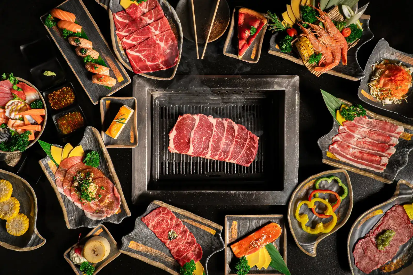 A charcoal grill with sliced beef, ringed by plates of wagyu, salmon, prawns and vegetables