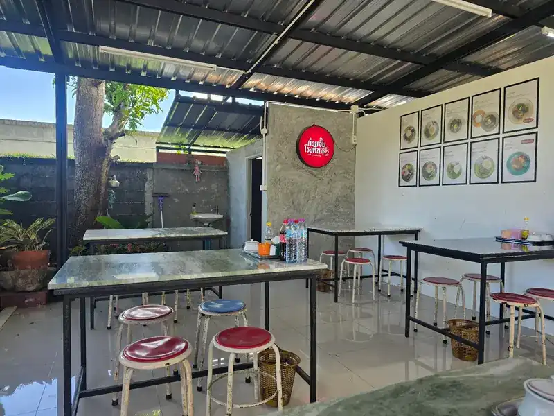The open-sided dining room under a tin roof, with marble tables, red stools and the round red sign on a concrete wall