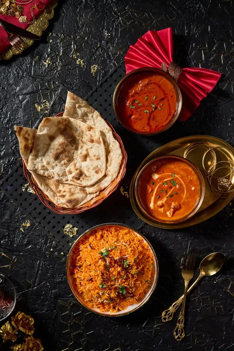 Two curries in brass bowls with a basket of flatbread and rice