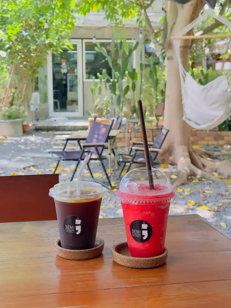 An iced black coffee and a red blended drink in Semicolon cups on a garden table, a hammock behind