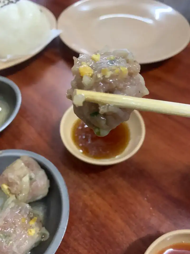 A dumpling lifted with chopsticks above a saucer of dipping sauce