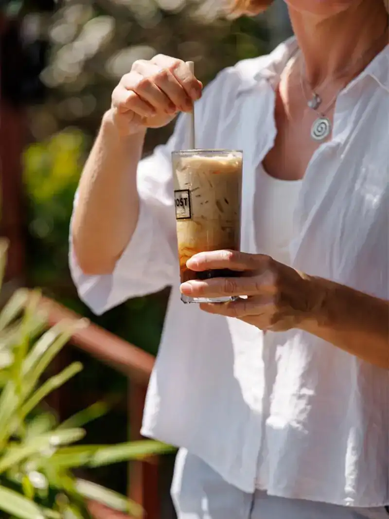 Hands stirring an iced latte in a BOOST glass on the terrace