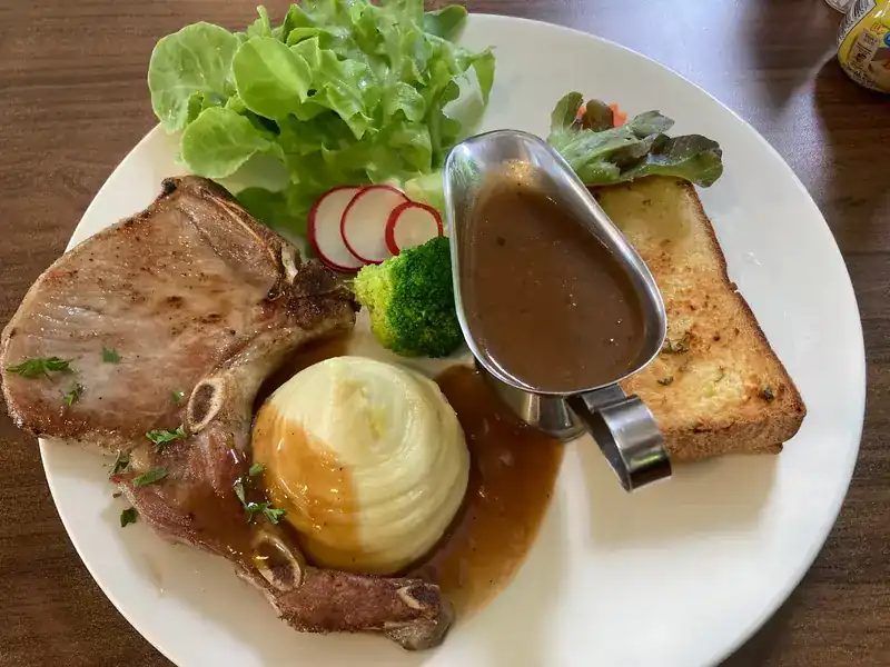 A grilled chop with a dome of mashed potato, gravy in a small jug, salad, radish and toast