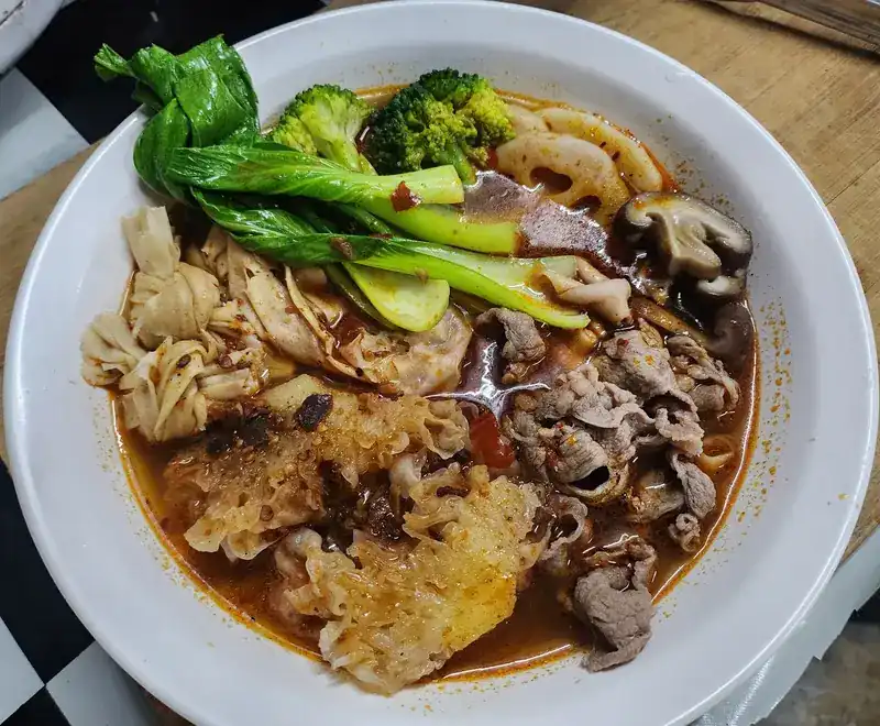 A bowl of beef soup with tripe, bok choy, broccoli, lotus root and shiitake mushrooms.