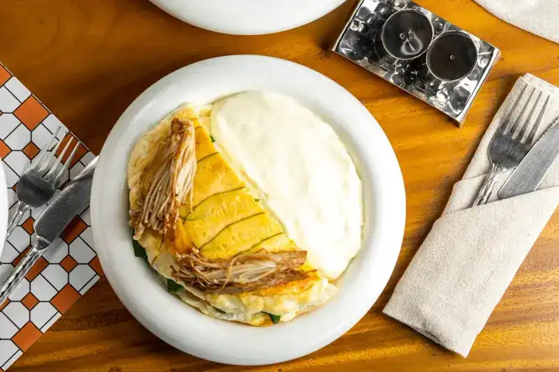 An omelette with mushrooms on a white plate, cutlery and a tiled napkin beside it