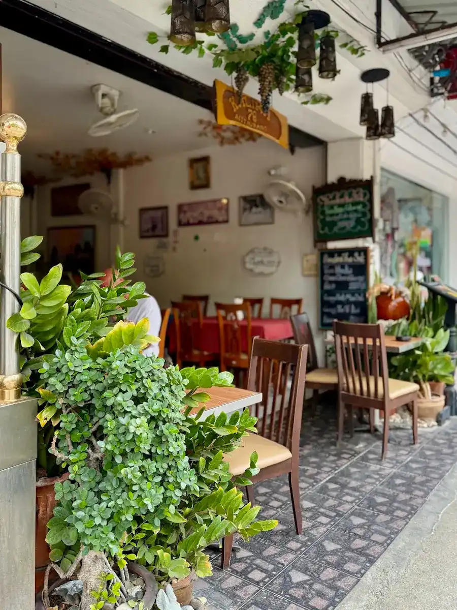 The front of Kalika restaurant: wooden chairs and tables on patterned tiles, potted plants, and chalkboards hanging by the door