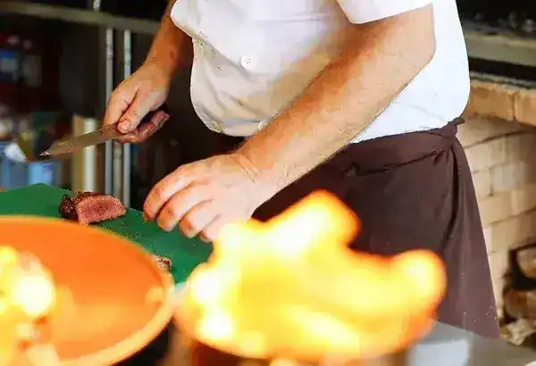 The chef's hands slicing grilled beef on a board