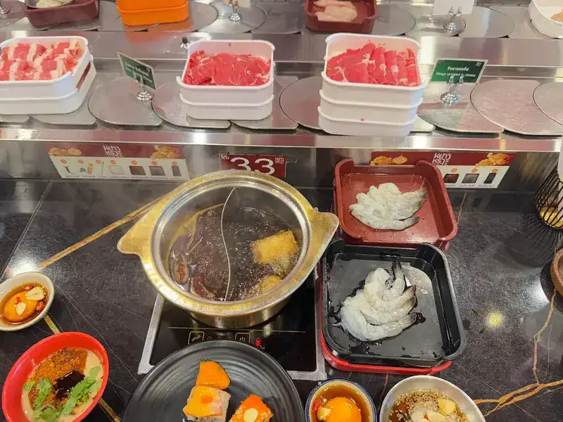 A split pot with two broths on the hotplate, with shrimp, sliced meat and dipping sauces around it
