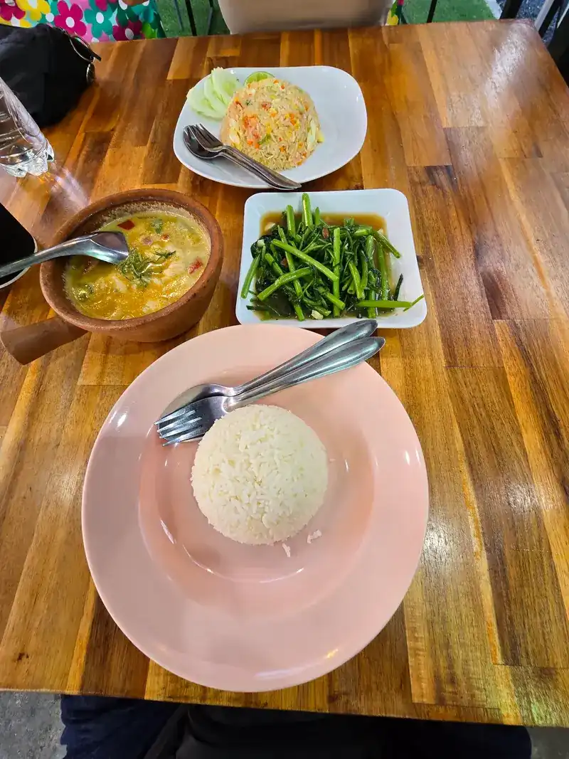 A Thai meal on a wooden table: soup in a clay bowl, stir-fried morning glory, fried rice and steamed rice / อาหารไทยบนโต๊ะไม้ ซุปในชามดินเผา ผัดผักบุ้ง ข้าวผัด และข้าวสวย