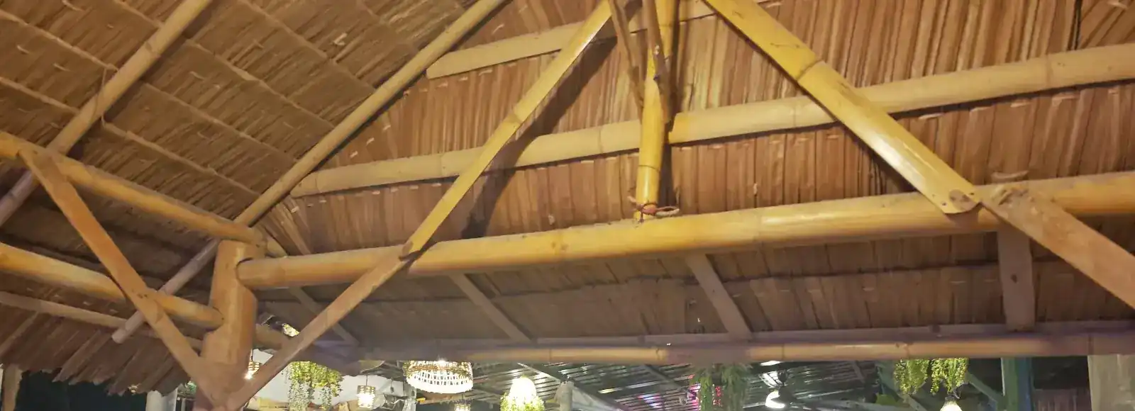 Thatched roof on bamboo beams over the tables, lamps lit for the evening