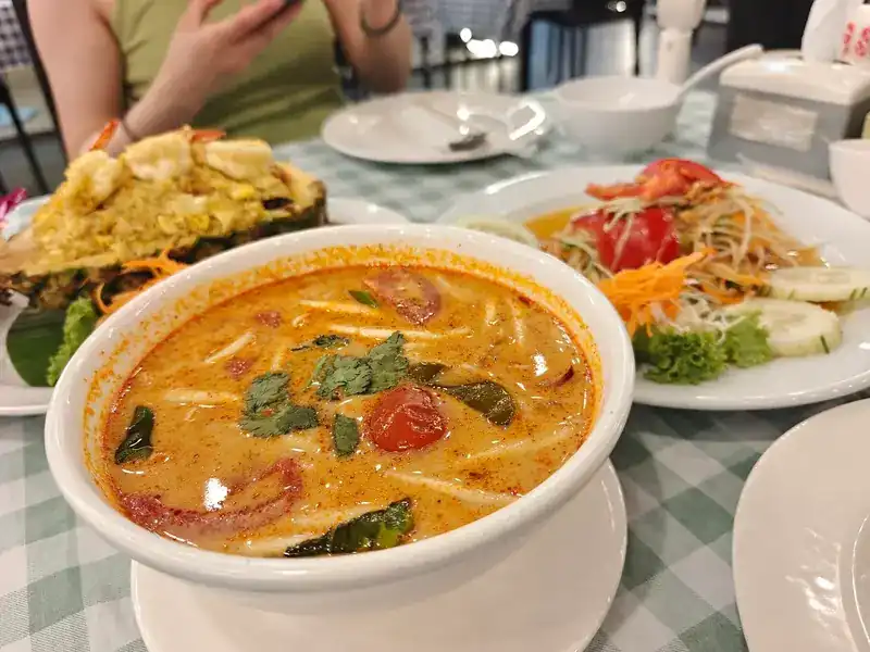 A creamy soup with tomato and herbs, pineapple fried rice and papaya salad on a green-check table