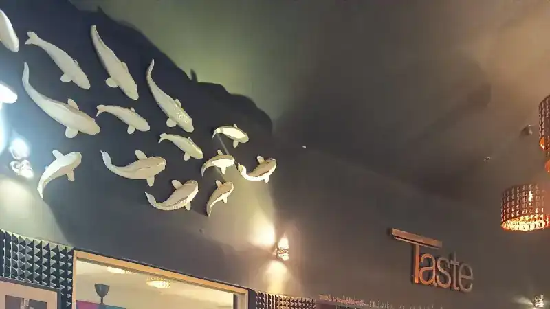 White koi fish sculptures swimming across a dark wall, beside the Taste sign