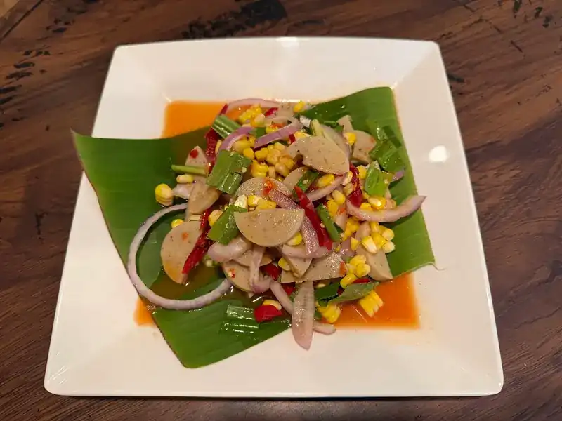 Spicy salad of sliced sausage with sweetcorn, red onion, celery and chilli, served on a banana leaf.