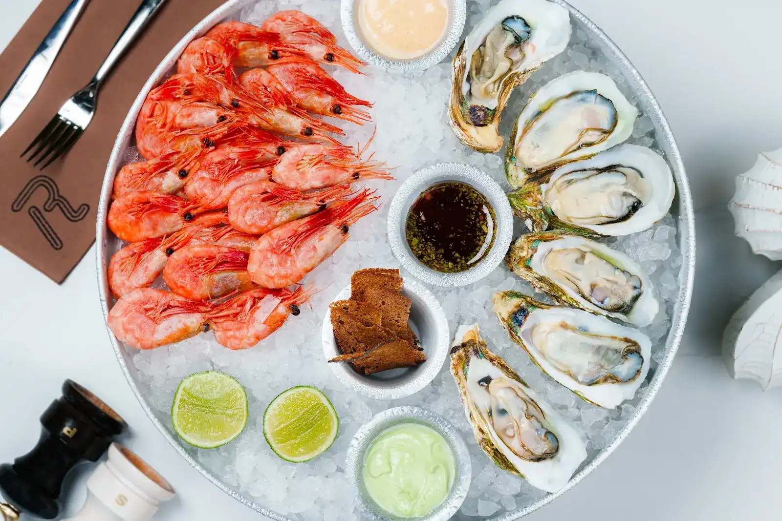 Oysters and Magadan shrimp on crushed ice with lime and three sauces, seen from above
