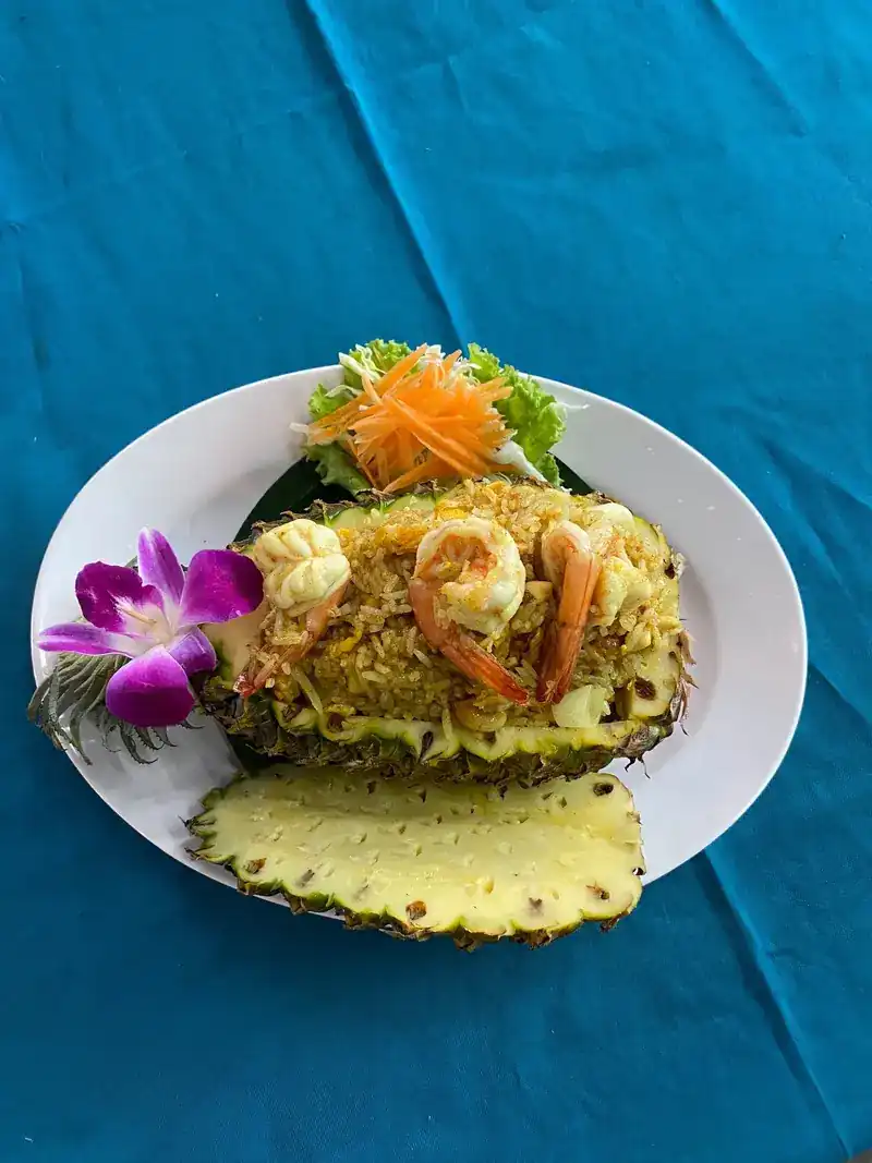 Pineapple fried rice with prawns in a pineapple half, garnished with an orchid