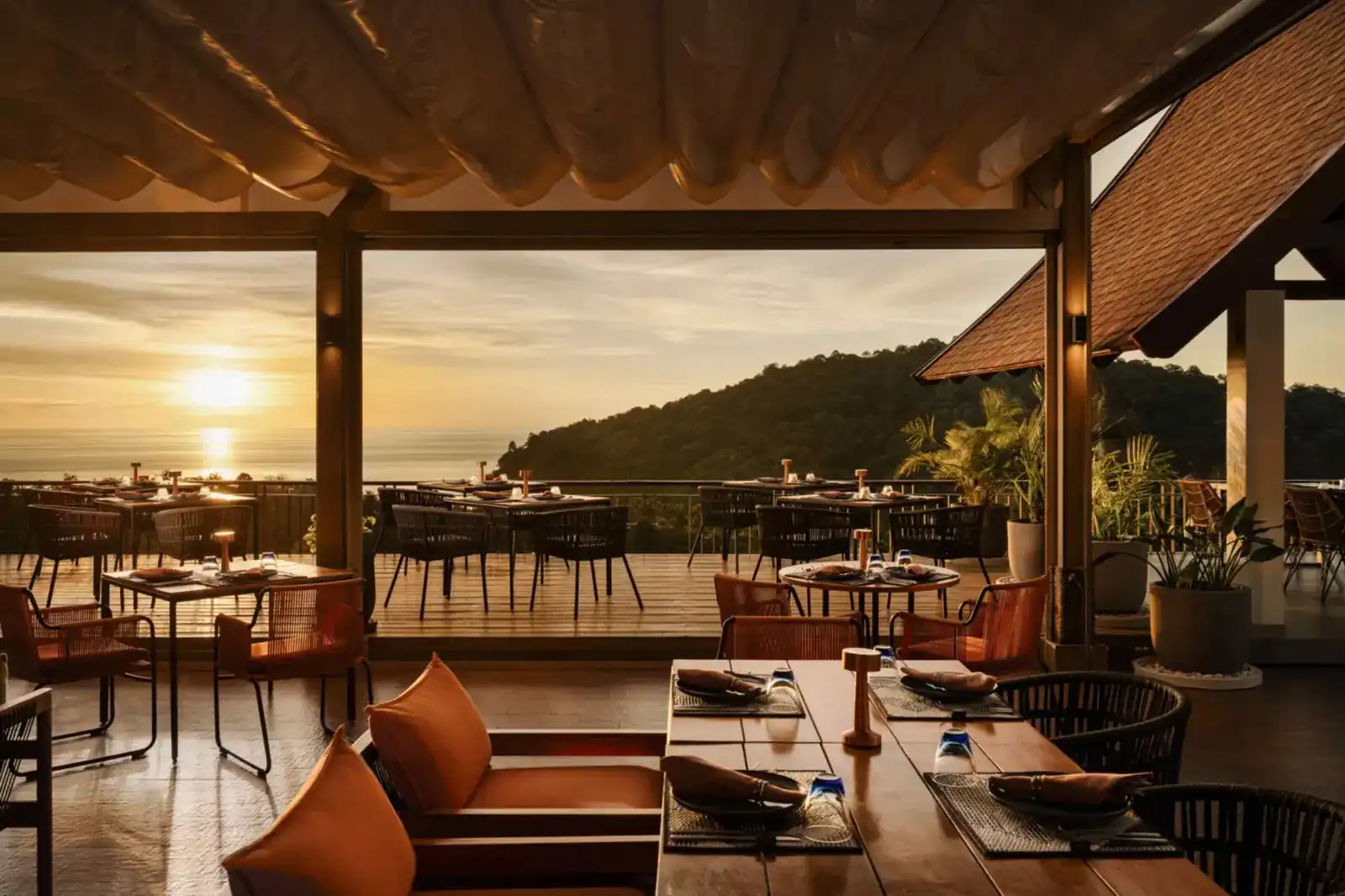 The rooftop terrace at sunset, tables set, the sea and a green headland beyond