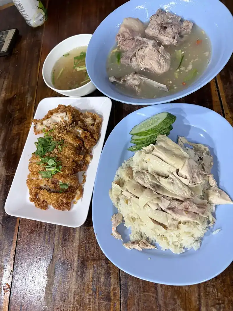 Chicken rice with cucumber, fried chicken and two bowls of soup on a wooden table