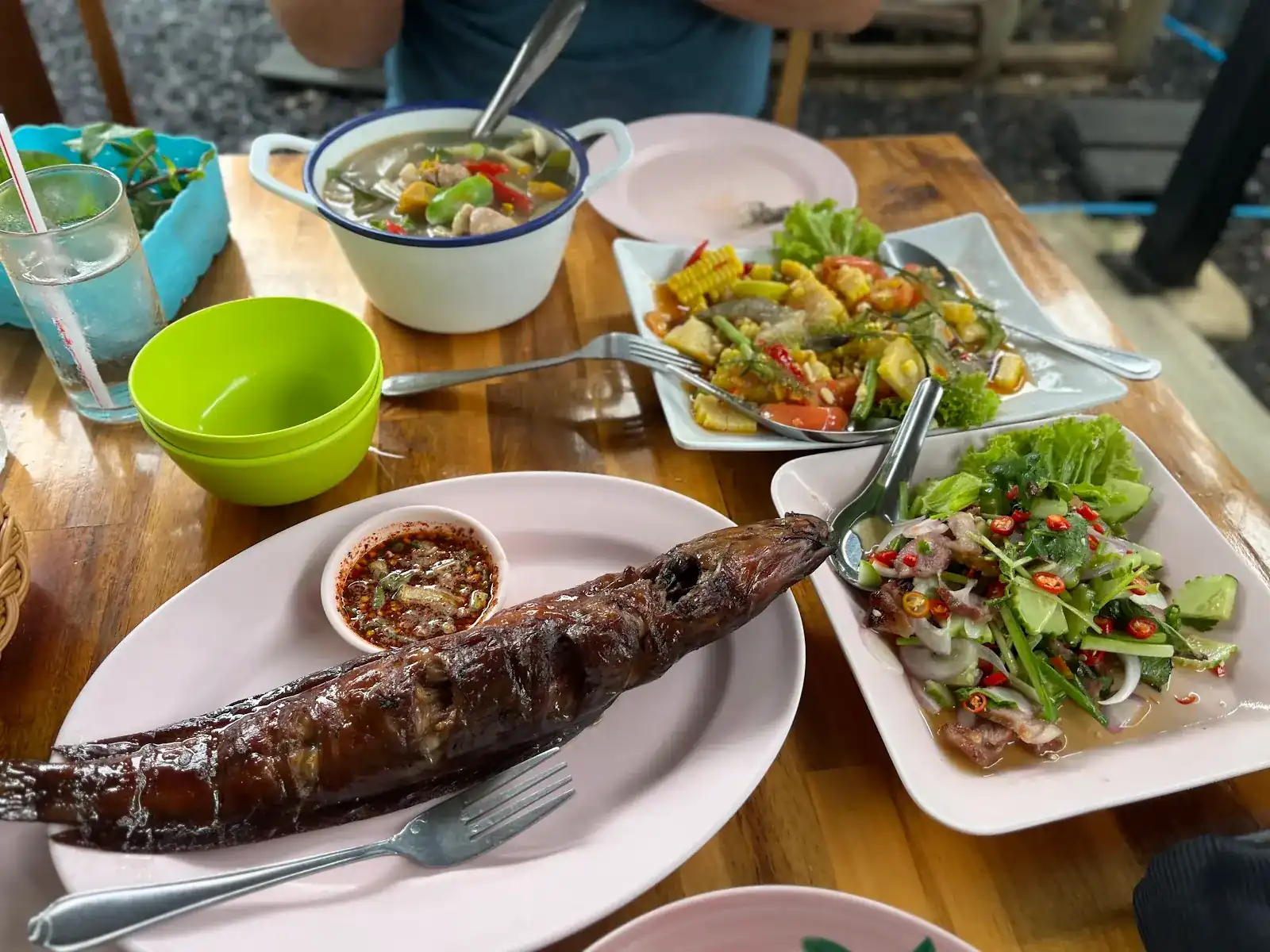 Grilled fish with a chilli dipping sauce, a sweetcorn salad, a spicy salad and a pot of soup on a wooden table