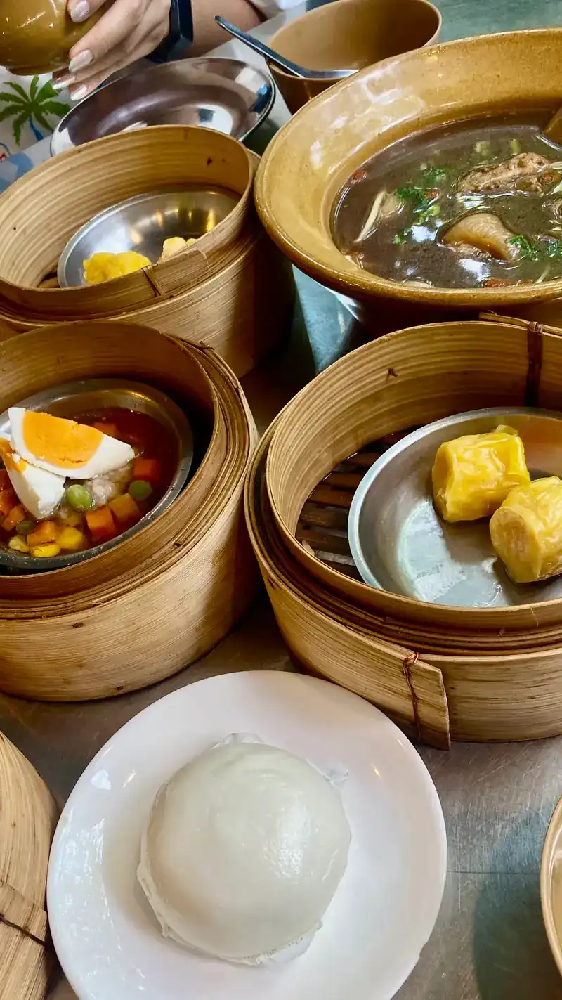 A table of dim sum: shumai, steamed pork with egg, a steamed bun and a bowl of soup