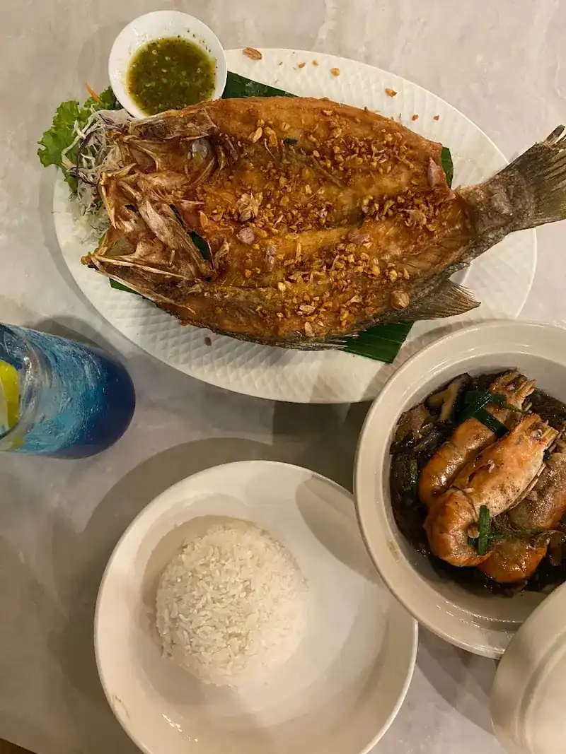 A whole fried fish covered in fried garlic, with a pot of prawns and a bowl of rice
