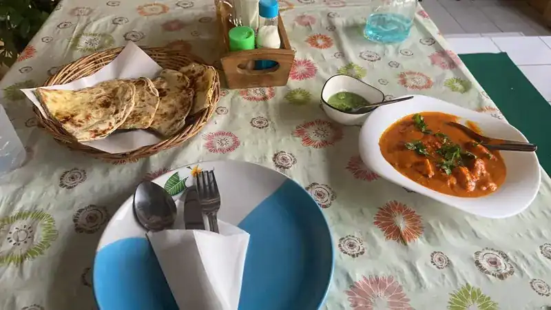 A basket of naan, a curry and green chutney on the table