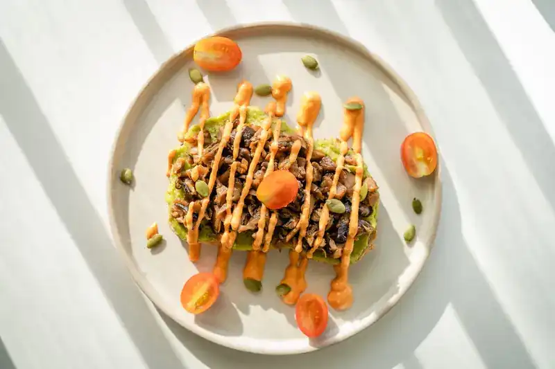 Toast with avocado and mushrooms on a plate in striped sunlight