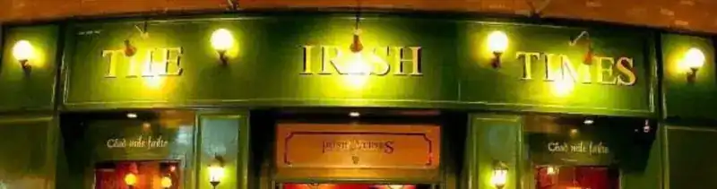 The green front of the Irish Times pub with brass letters and wall lamps