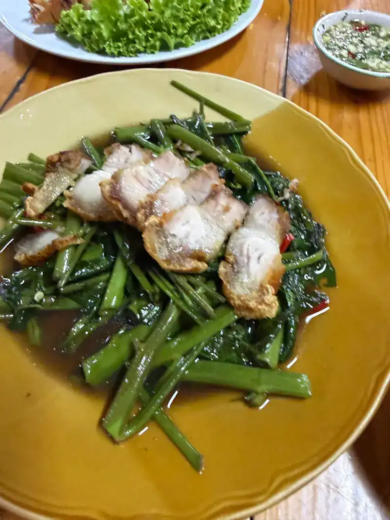 Stir-fried morning glory topped with slices of crispy pork