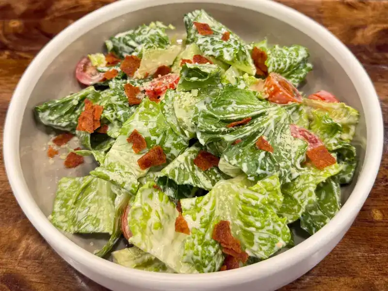 A bowl of green salad with creamy dressing, cherry tomatoes and crisp toppings
