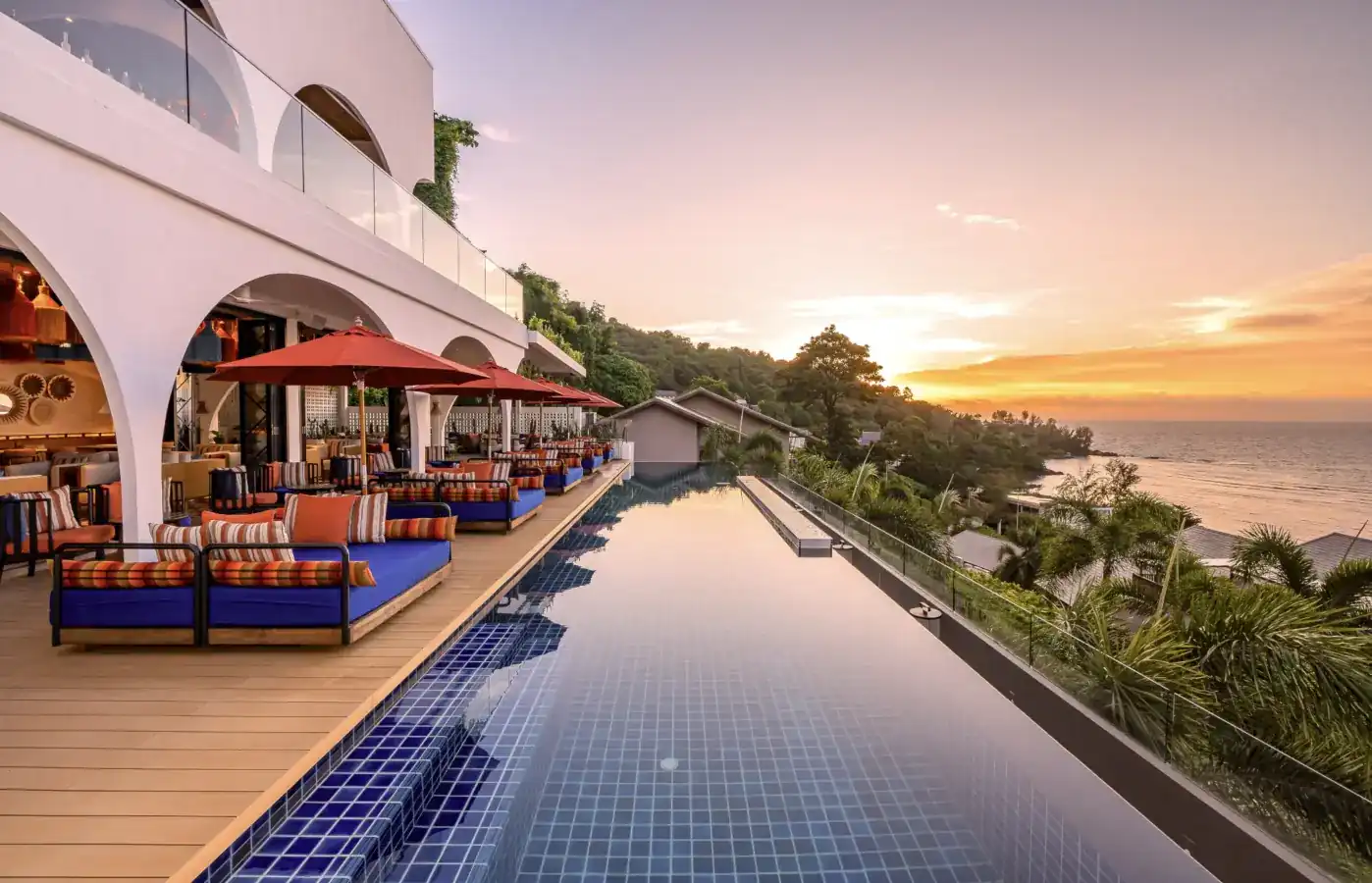 The infinity pool and daybeds under the white terraces of Casa Boho at sunset, with Kamala Bay beyond