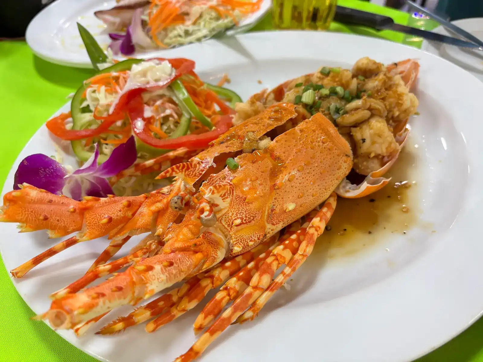 A split lobster, cooked and served with salad and an orchid, on a lime-green tablecloth