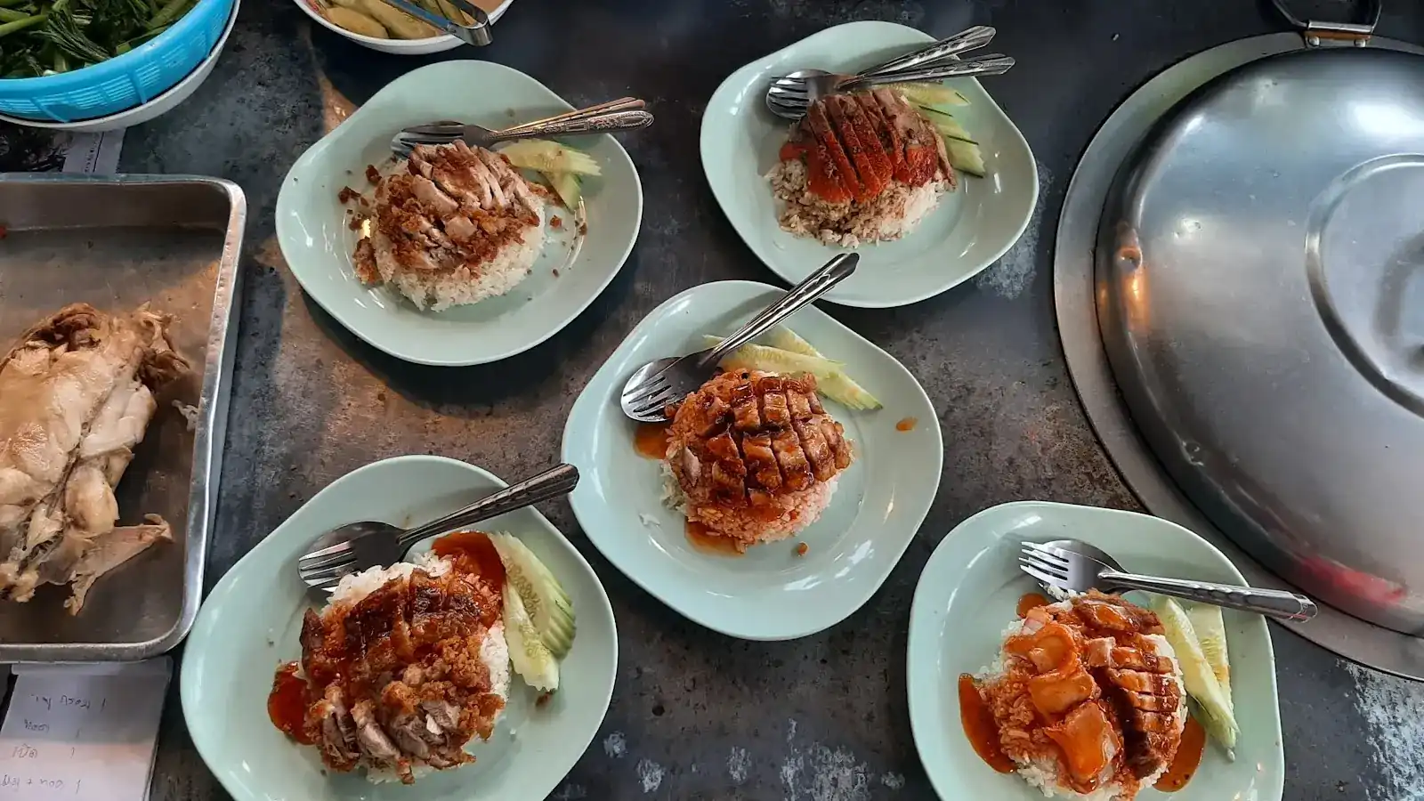 Plates of rice with roast duck, red pork and crispy pork, with cucumber, on the steel counter