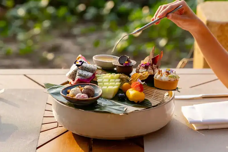 A shared platter of small desserts and cut fruit on a banana leaf
