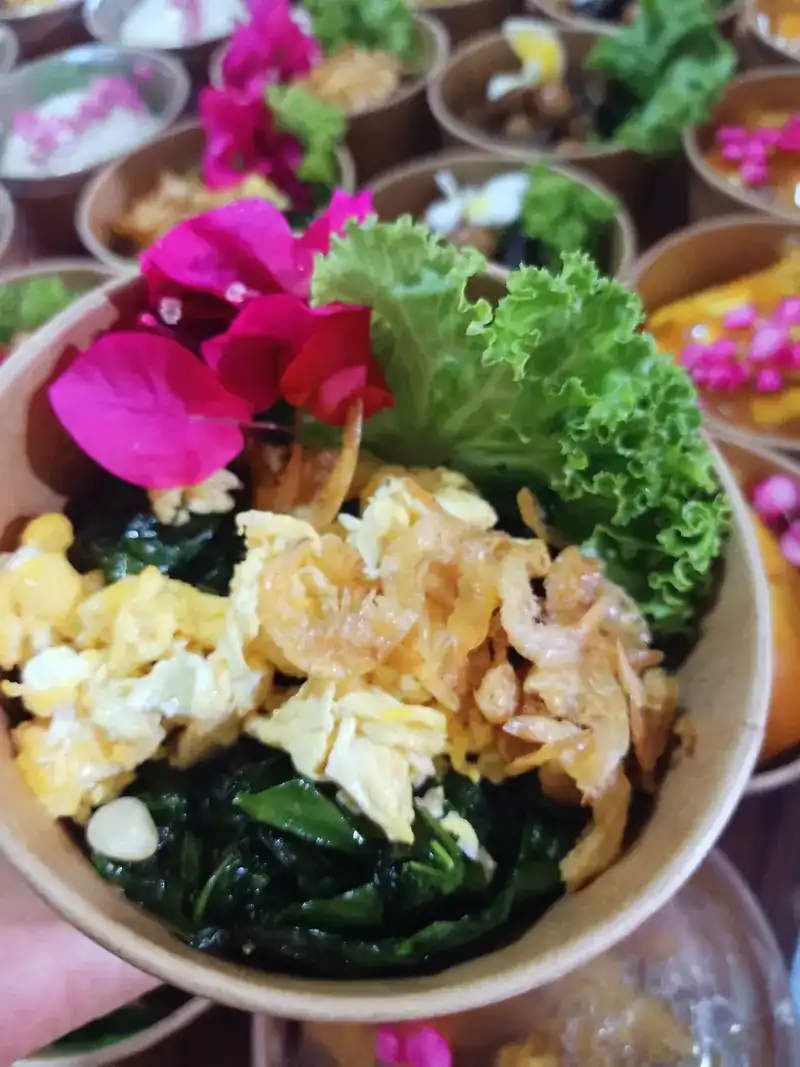 A bowl of stir-fried greens with egg and dried shrimp, with lettuce and pink flowers on top