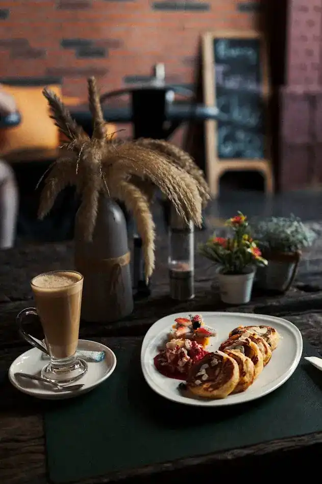 A latte and pancakes with berry sauce on a dark wooden table