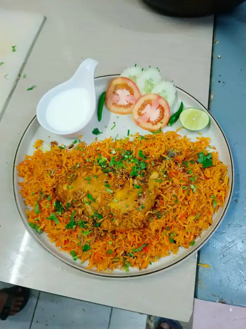Biryani rice heaped on the plate with yogurt, tomato, cucumber, chilli and lime