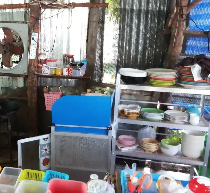The kitchen: a wall fan, tin walls and shelves of coloured plates