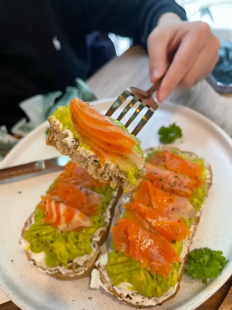 Two slices of avocado toast topped with salmon on a white plate