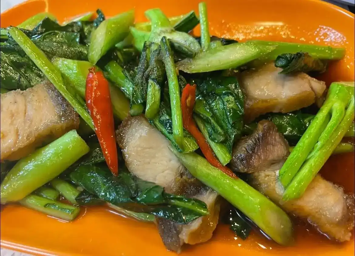 Kale stir-fried with slices of pork belly and red chilli on an orange plate