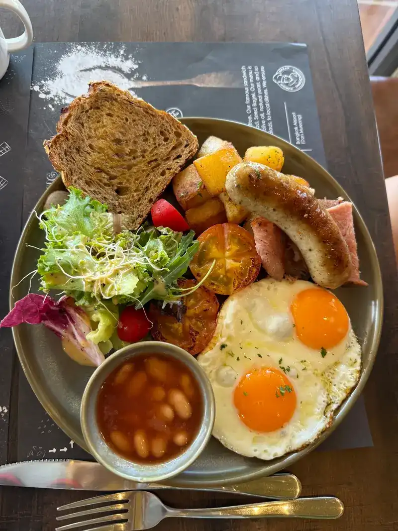 A breakfast plate with two fried eggs, sausage, baked beans, potatoes, salad and toast
