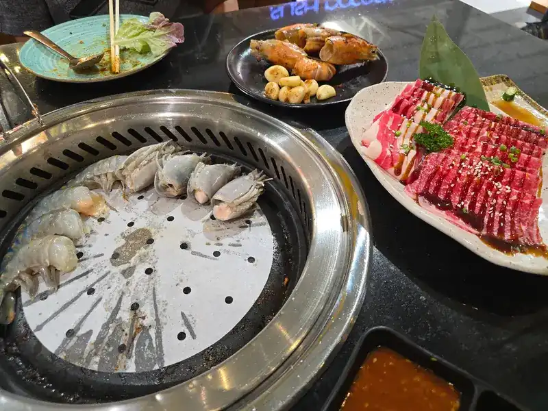 Prawns on the table grill, with a plate of sliced wagyu beside it