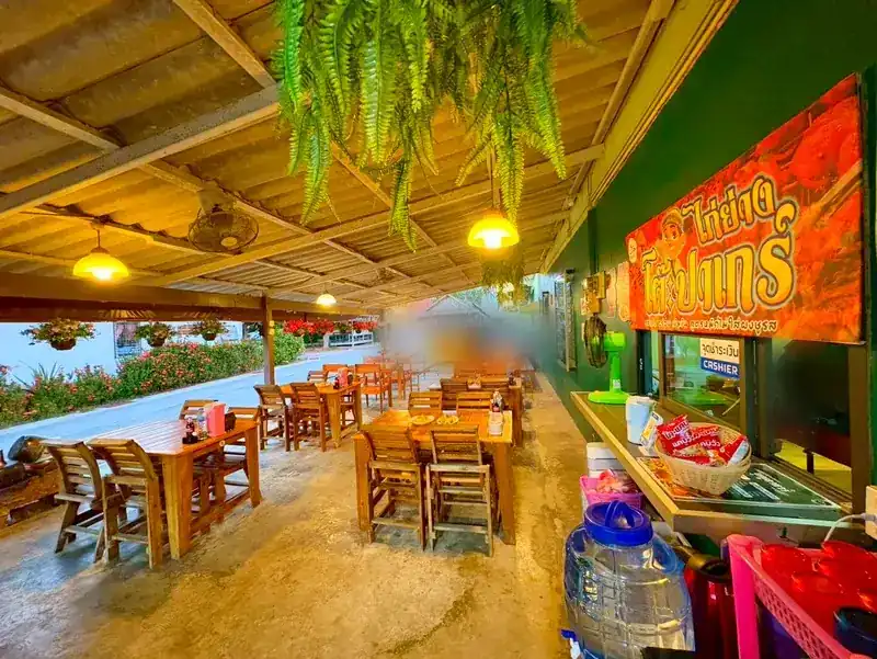 Wooden tables and chairs under a covered terrace with hanging ferns and the shop sign