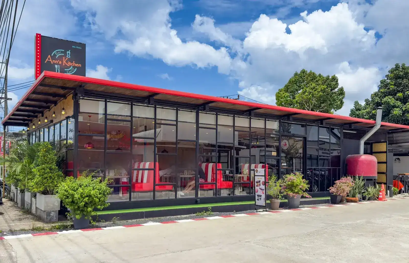 Ann's Kitchen seen from the road: a long glass-walled diner under a red roof, red-and-white booths inside, potted plants along the front