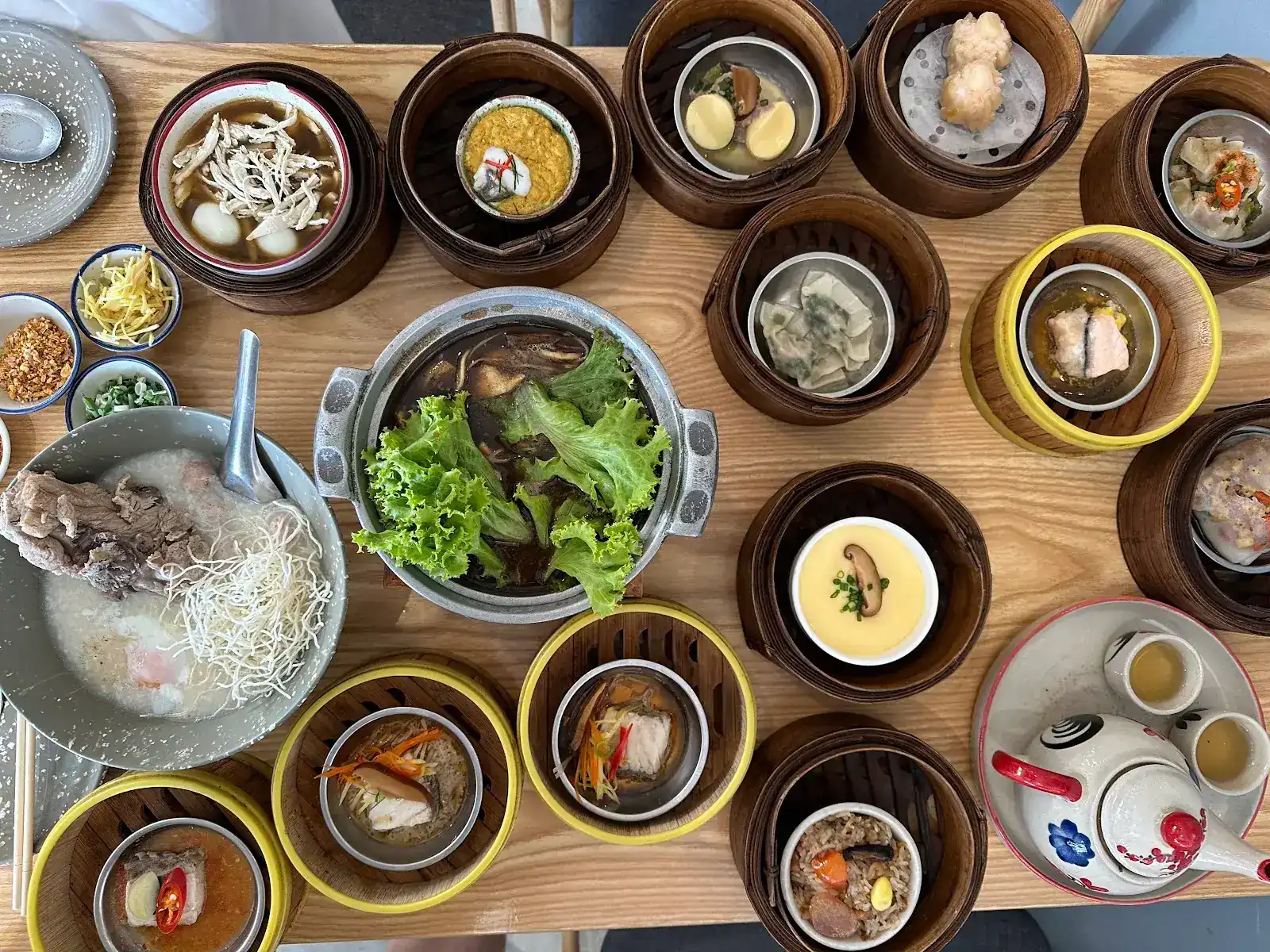 Dim sum in bamboo baskets around a pot of bak kut teh, with rice porridge, steamed egg and a pot of tea, seen from above