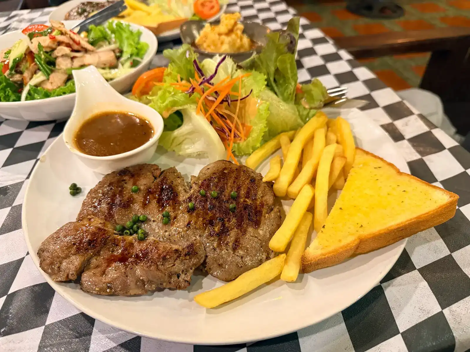 Steak with green peppercorns, fries, garlic toast and salad on a black-and-white checked tablecloth