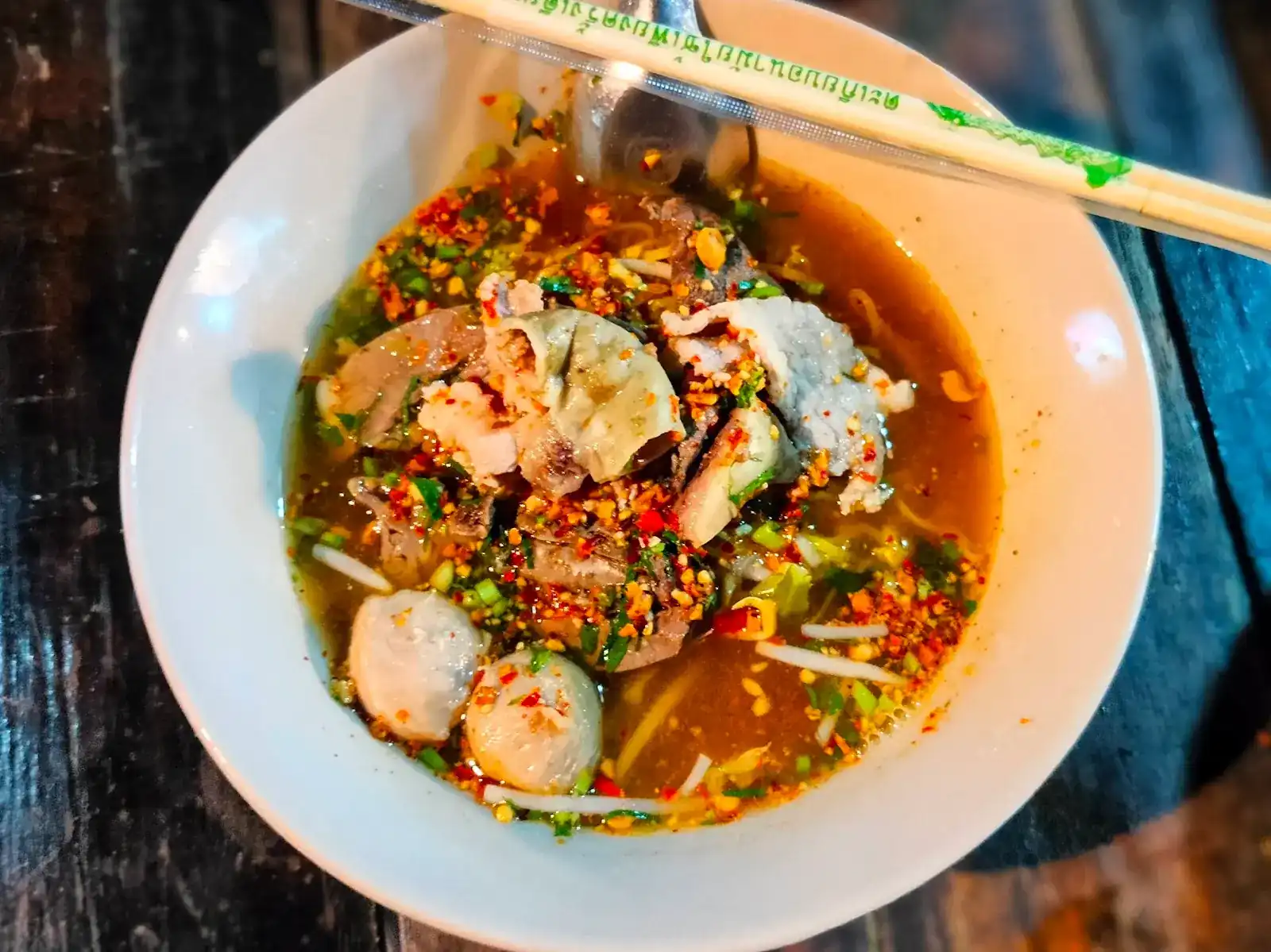 Noodle soup with sliced pork, meatballs, chilli flakes and crushed peanuts, chopsticks across the bowl