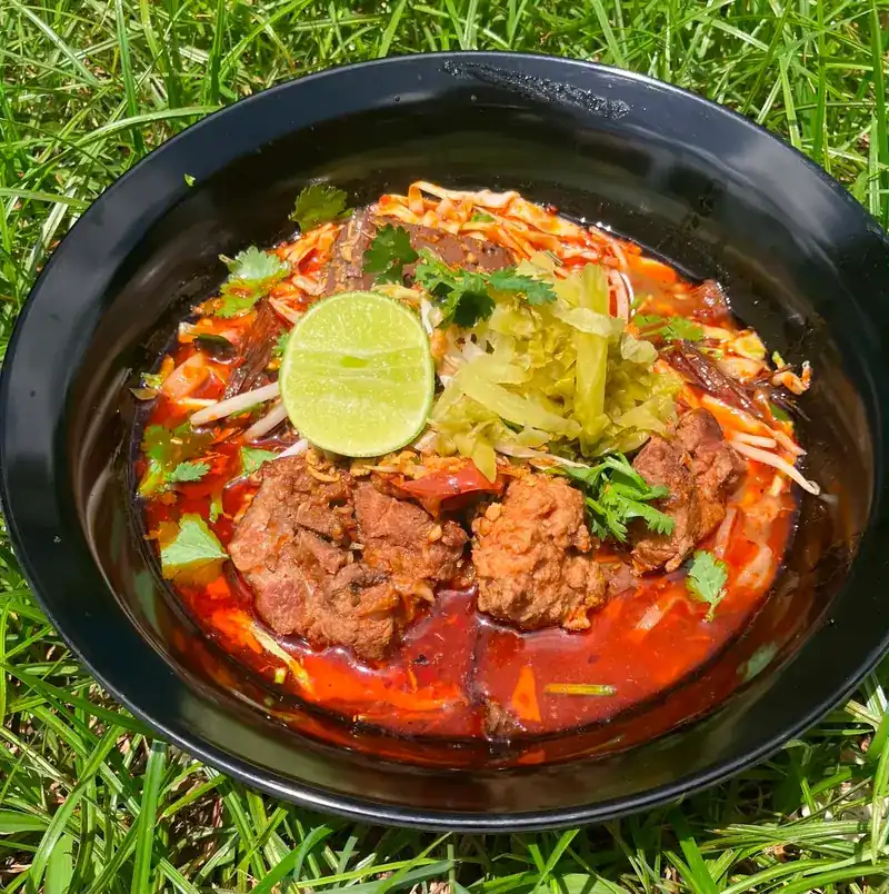 Noodles in a red curry broth with braised meat, bean sprouts, pickled greens and lime