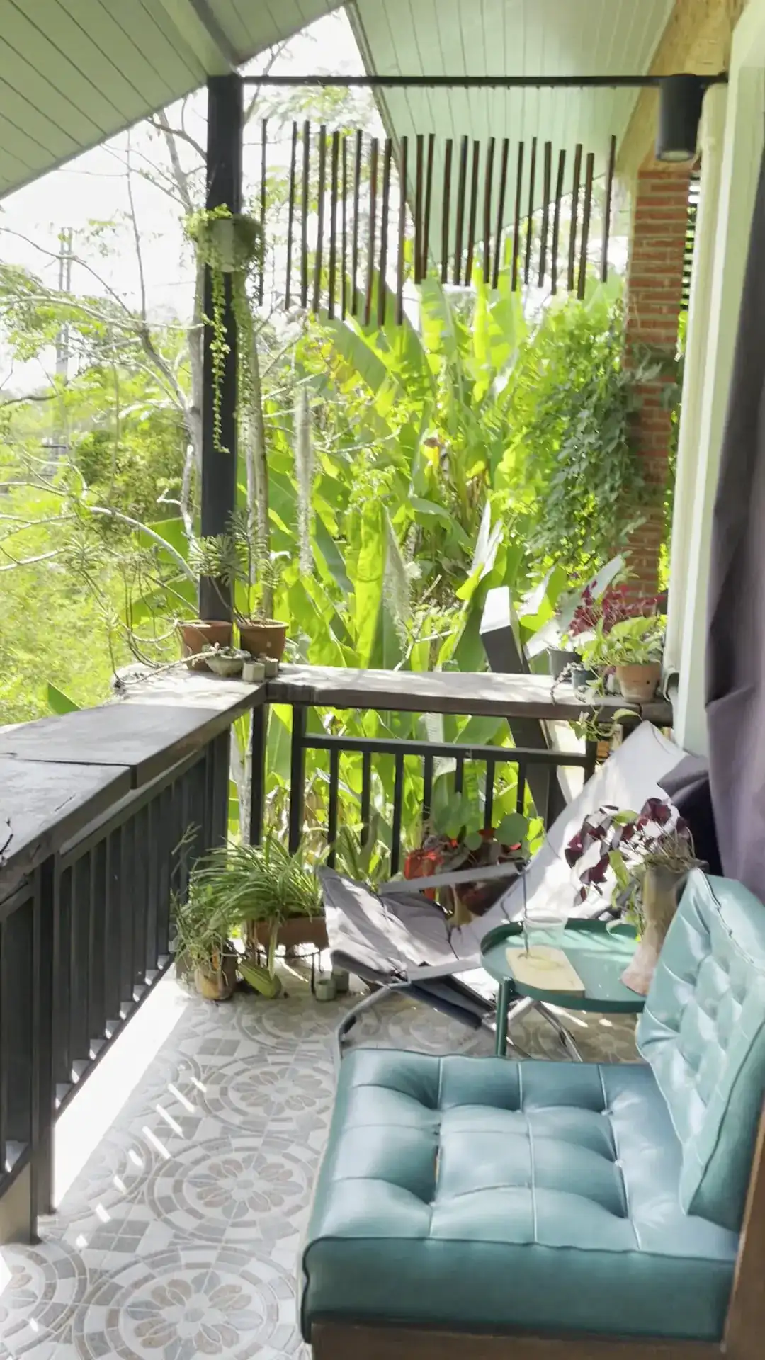 A teal leather armchair on the balcony, with banana plants and trees beyond the railing